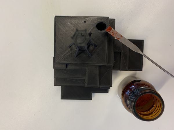 In der Abbildung ist das 3D-Modell des Kernkraftwerks Tschernobyl von oben dargestellt. Für den Versuch zur Ausbreitung von ionisierender Strahlung wird in das Loch im Modell mit einem Spatel fluoreszierende Farbe gegeben.